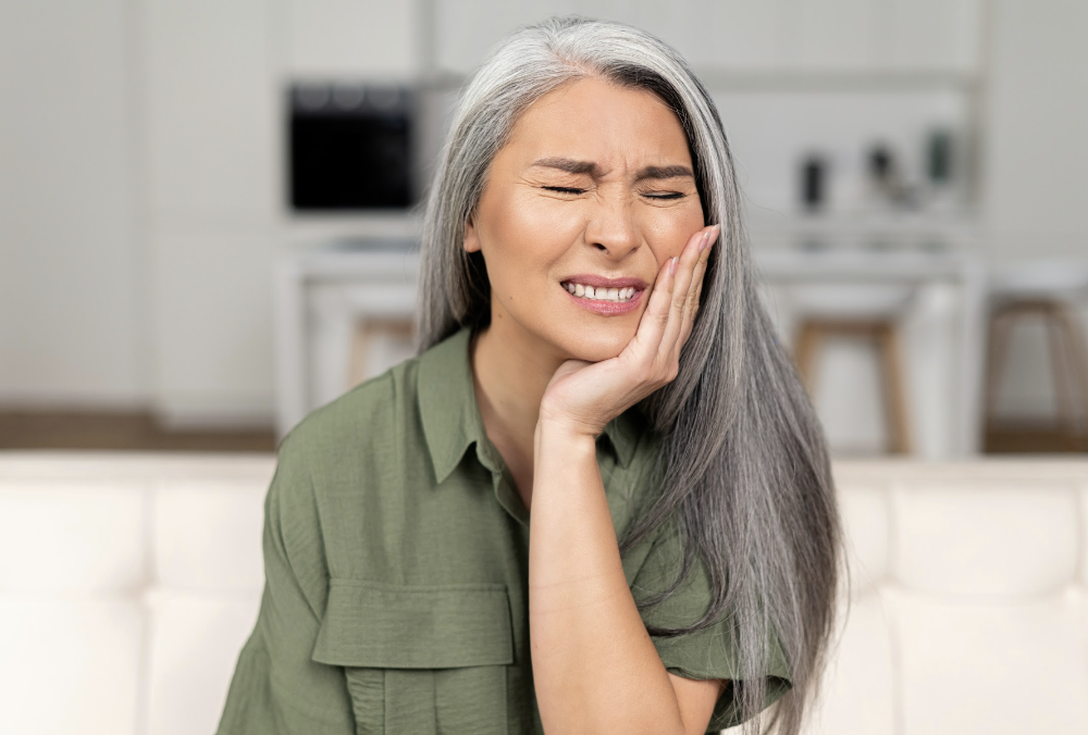 A woman with a pained expression on a couch, experiencing a toothache and in need of emergency dental assistance