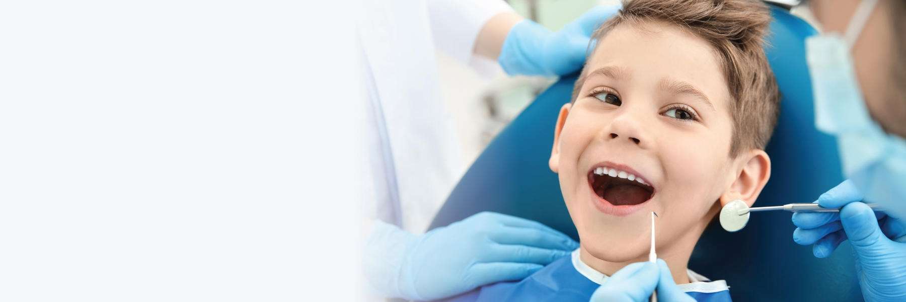 A child sits in a dental chair while a dentist wearing blue gloves examines their teeth with dental instruments, representing a professional and caring children's dentistry environment.