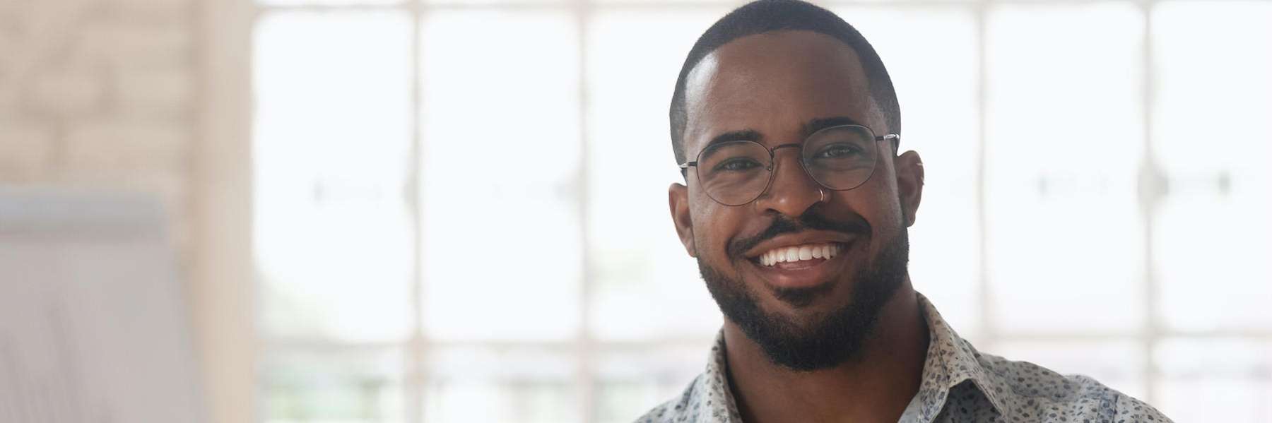 A cheerful man in glasses and a shirt, representing Root Canal Therapy with a welcoming smile.