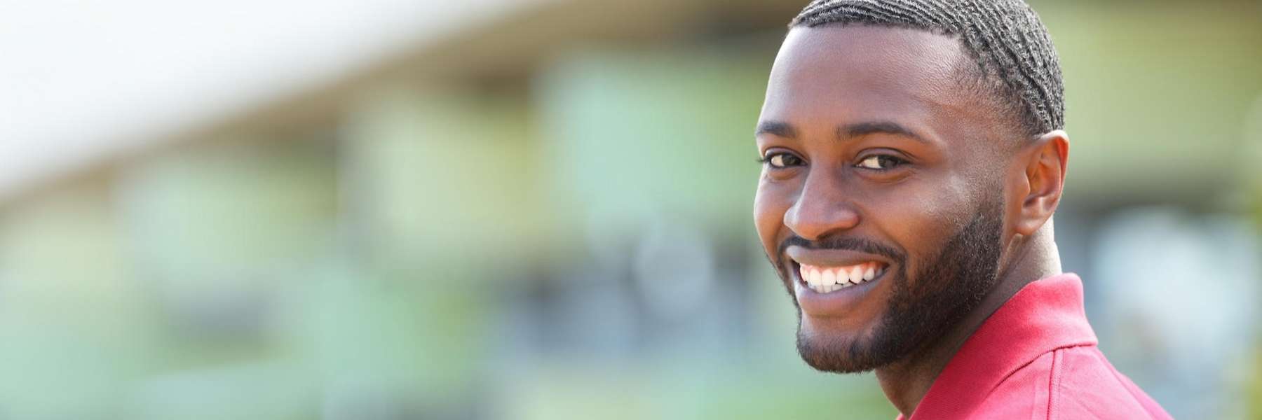 A smiling man in a red shirt poses for the camera, radiating warmth and friendliness.